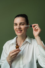 A nice woman with clean skin should apply oil, essence from a pipette to her face.