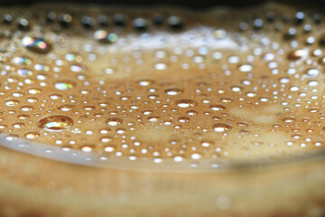 Closeup of bubbles texture of hot coffee on rim of glass.