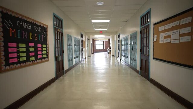 Wide angle push in down a long empty high school corridor hallway lined with student lockers.