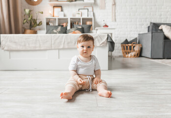 Portrait of a 7-9 month old baby in a home interior. A curious, smiling child explores the world around him. A cute baby is sitting on the floor.