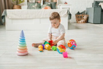 baby 6-9 months old playing with a colorful rainbow toy pyramid sitting in a white sunny bedroom. Toys for small children. Children's interior. A child with an educational toy.