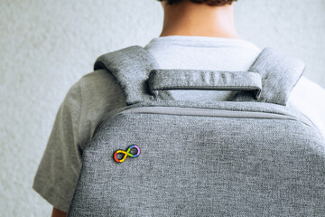 Teenage boy with autism infinity rainbow symbol sign metallic pin brooch on gray backpack. World...