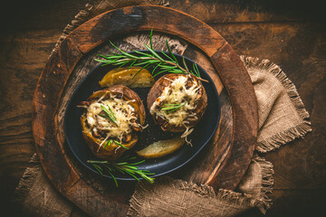 Two baked potatoes with mushrooms, sour cream and cheese on a rustic wooden background