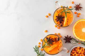 Cups of sea buckthorn tea with orange, berries, cinnamon and rosemary on white table. Healthy herbal autumn drink