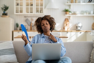 Sweaty African American millennial girl suffer from heat while working remotely at home, sitting on...