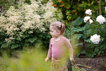 toddler girl staying among the greenery in the garden, children activity outdoor, healthy growing up