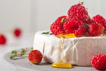 Camembert cheese with fresh raspberries, strawberries, honey and thyme on white background. French appetizer