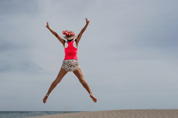 Obraz premium a woman jumping in front of the sea on the beach. concept of victory, success and freedom.