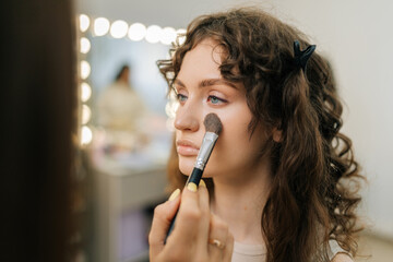 Closeup face of young woman being given applying highlighter for facial sculpting from...