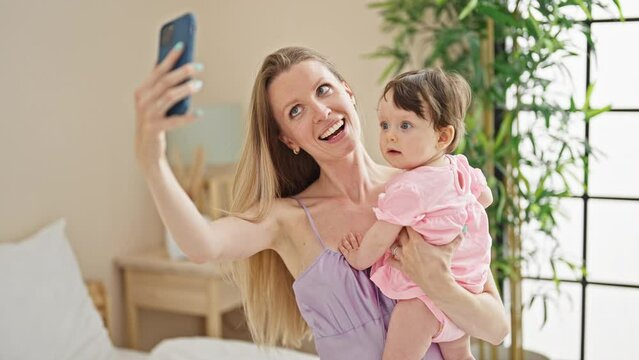 Mother and daughter sitting on bed make selfie by smartphone at bedroom