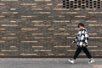 young man walks down the street in front of a brick wall