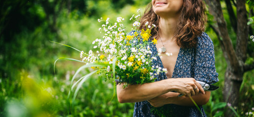 Young cheerful smiling woman in summer dress holding a bouquet of wildflowers in a summer garden