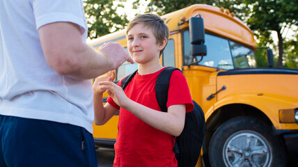 a boy stands with his dad in front of a yellow school bus. father walks his son to the bus to...