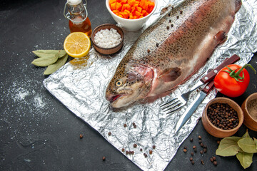 Above view of scales removed fresh fish cutlery set oil bottle bay leaves tomato lemon and different spices on dark color table