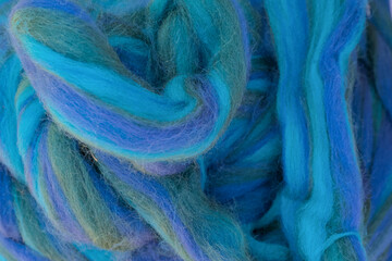 Multicolored blue strings of wool for felting and spinning as a background.
