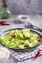 Spicy salad of cucumber slices, hot red pepper and sesame seeds on a plate vertical view
