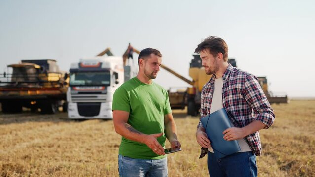 Farmer and agronomist shaking hands in wheat field after agreement. Agriculture business contract concept. Corporate farmer and landlord rancher negotiate with handshake. Combine harvesters harvest.