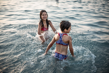 two standing girls in bikini playing with water in the sea