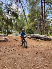 young Cyclist Riding the Bike on the Trail in the Pine Forest