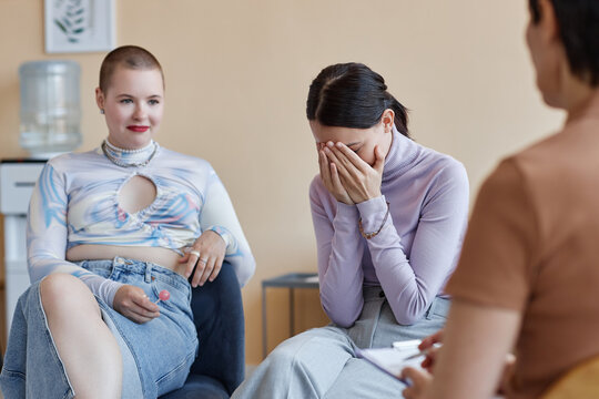 Sad young woman discussing her problems in group together with psychologist