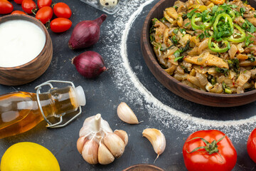 Close up view of eggplant dish served with green flour spices vegetables fallen oil bottle on black background