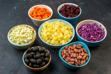 Front view of set of chopped fresh foods in bowls on dark color background with free space