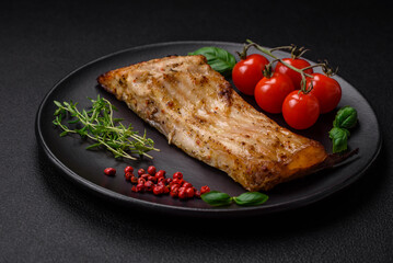 Slice of delicious baked fish with salt, spices and herbs on a ceramic plate