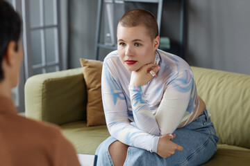 Young woman sitting on sofa and listening to psychologist during consultation in office