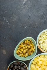 Half shot of set of chopped fresh foods in bowls on dark color background in vertical view