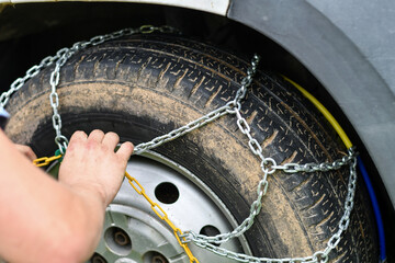 Man hand wrapping car wheel with anti slip chain for climbing up dirt road. Close-up.  Selective...