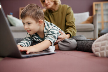 Closeup of curious excited boy with down syndrome using laptop on floor at home, copy space