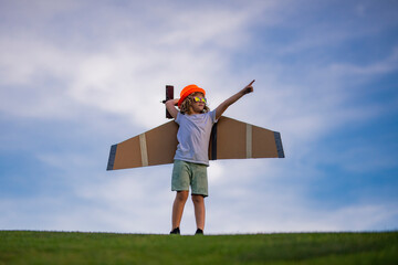 Child pilot aviator with with paper wings or toy airplane dreams of traveling in summer in nature.
