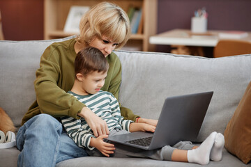 Side view portrait of mother and son with down syndrome using laptop together while sitting on sofa