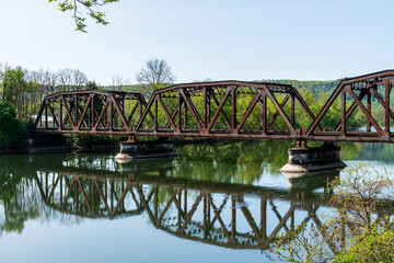 An old, rusted railroad bridge over the Allegheny River with it's reflection on the water in Warren, Pennsylvania, USA on a sunny spring day