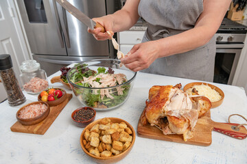 woman in a home kitchen adds chicken pieces to a delicious caesar salad.