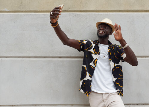 Cheerful black man taking selfie and waving hand