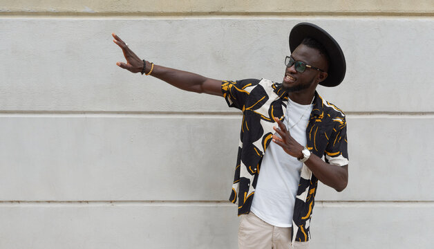 Cheerful trendy black guy dancing against wall on street