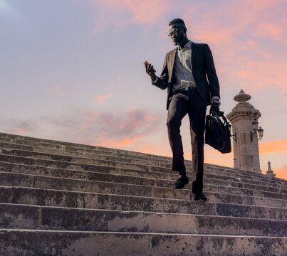 Stylish young black businessman with smartphone and briefcase walking downstairs