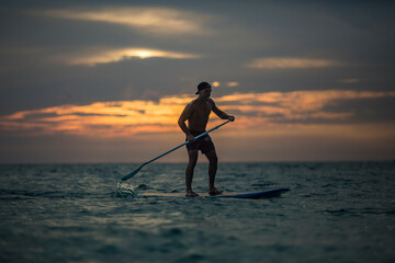 Active male surfer balancing on standup paddleboard in sea