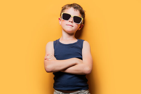 Stylish boy in sunglasses with crossed arms in studio