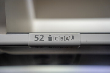 Close up on  52 A, B, C  row and seat identifier on an overhead bin of a commercial passenger aircraft.