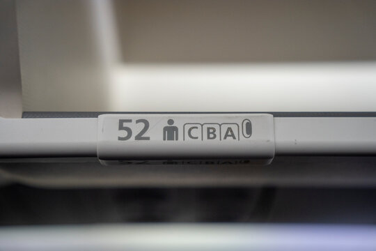 Close up on  52 A, B, C  row and seat identifier on an overhead bin of a commercial passenger aircraft.