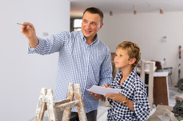 Adult man and preteen boy holding documents and talking in new house, planning design projects