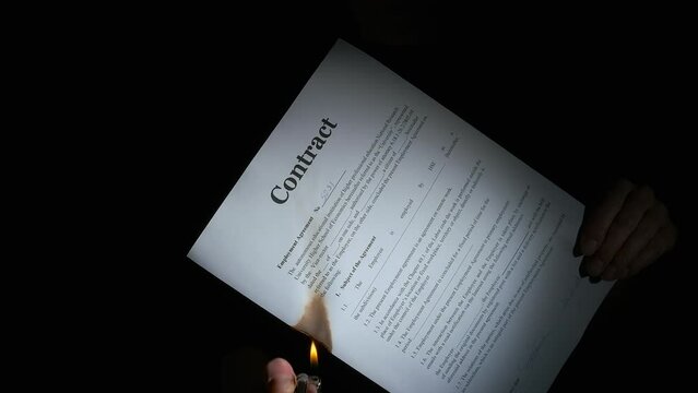 Burn the contract on black background. A view of burning contract documents in person hands on the black background. A concept of the end of agreement.