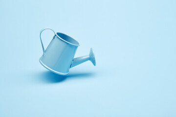 Bright blue garden watering can hover over the surface of the bright solid fond plain bright blue background