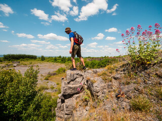 Slim athletic man on edge of a cliff, beautiful nature scene on a warm sunny day. Outdoor activity. Get out of town and adventure concept. Blue cloudy sky. Be active theme