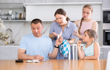 Obraz na płótnie Canvas Dissatisfied husband and father give out pocket money to wife and children in home kitchen