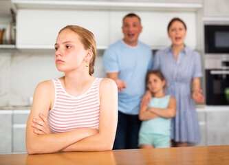 At home kitchen, parents scold daughter for careless act. Sulky preschool girl sit near table during serious conversation with parents