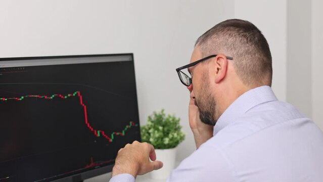 A frustrated or tired stock trader looks at the value is falling on the monitor screen. Bitcoins, futures, investment market. Bitcoins, futures, investment market.