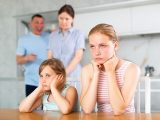 Confused upset daughters sitting at home cover ears with hands during mom and dad quarrel. Children...